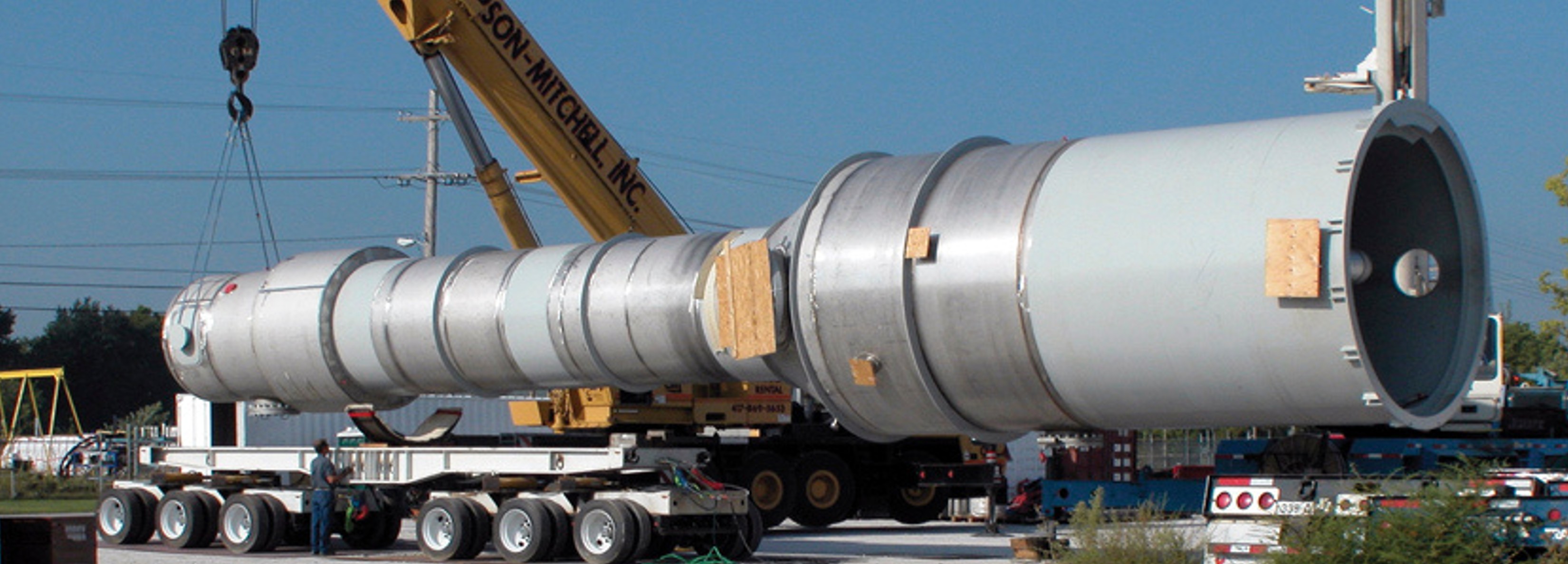 A tall fabricated process column staged on multi-axle transport trailers