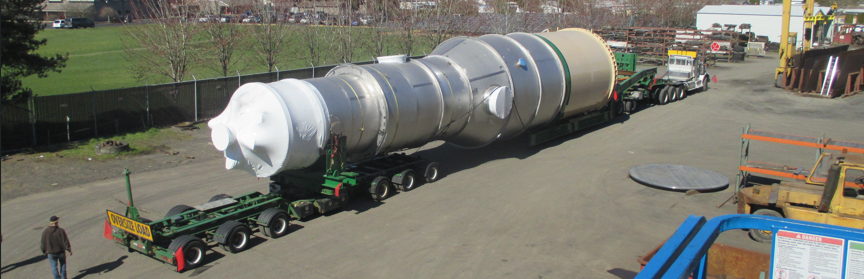 A tall fabricated process column staged on multi-axle transport trailers